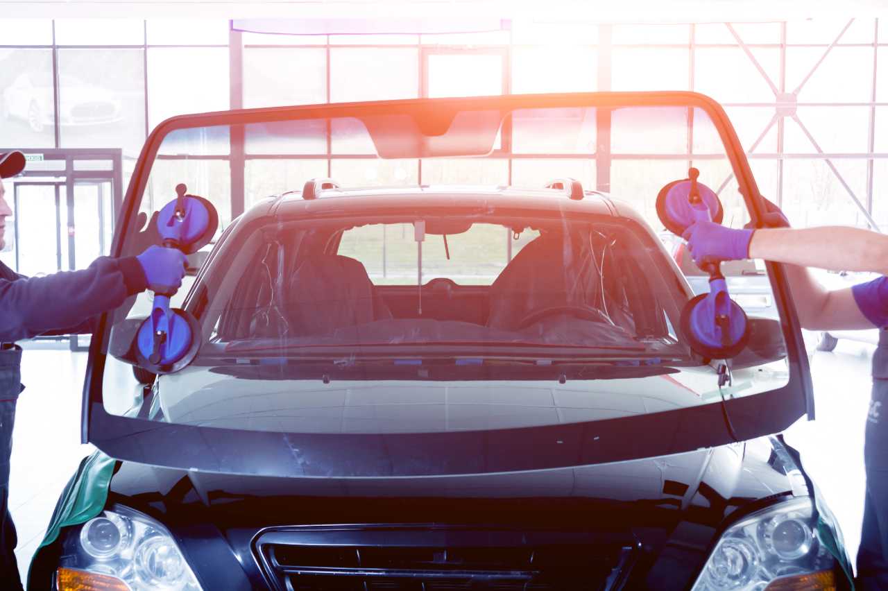 Automobile special workers replacing windscreen or windshield of a car in auto service station garage.